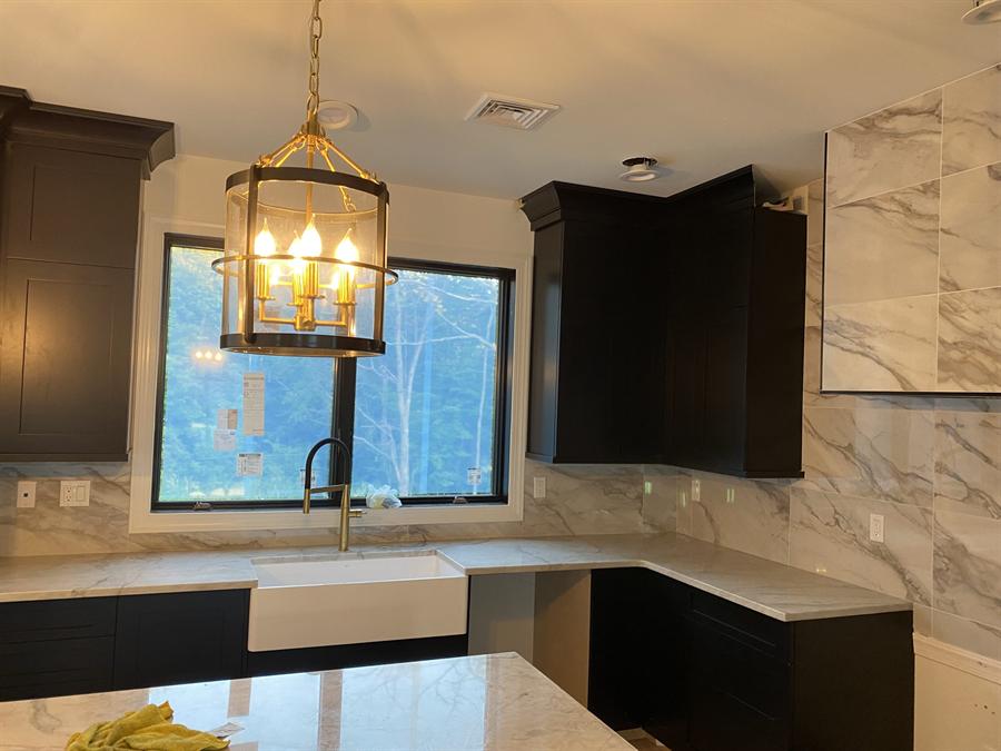 Dark cabinet kitchen with veined porcelain backsplash and brass pendant, New Jersey